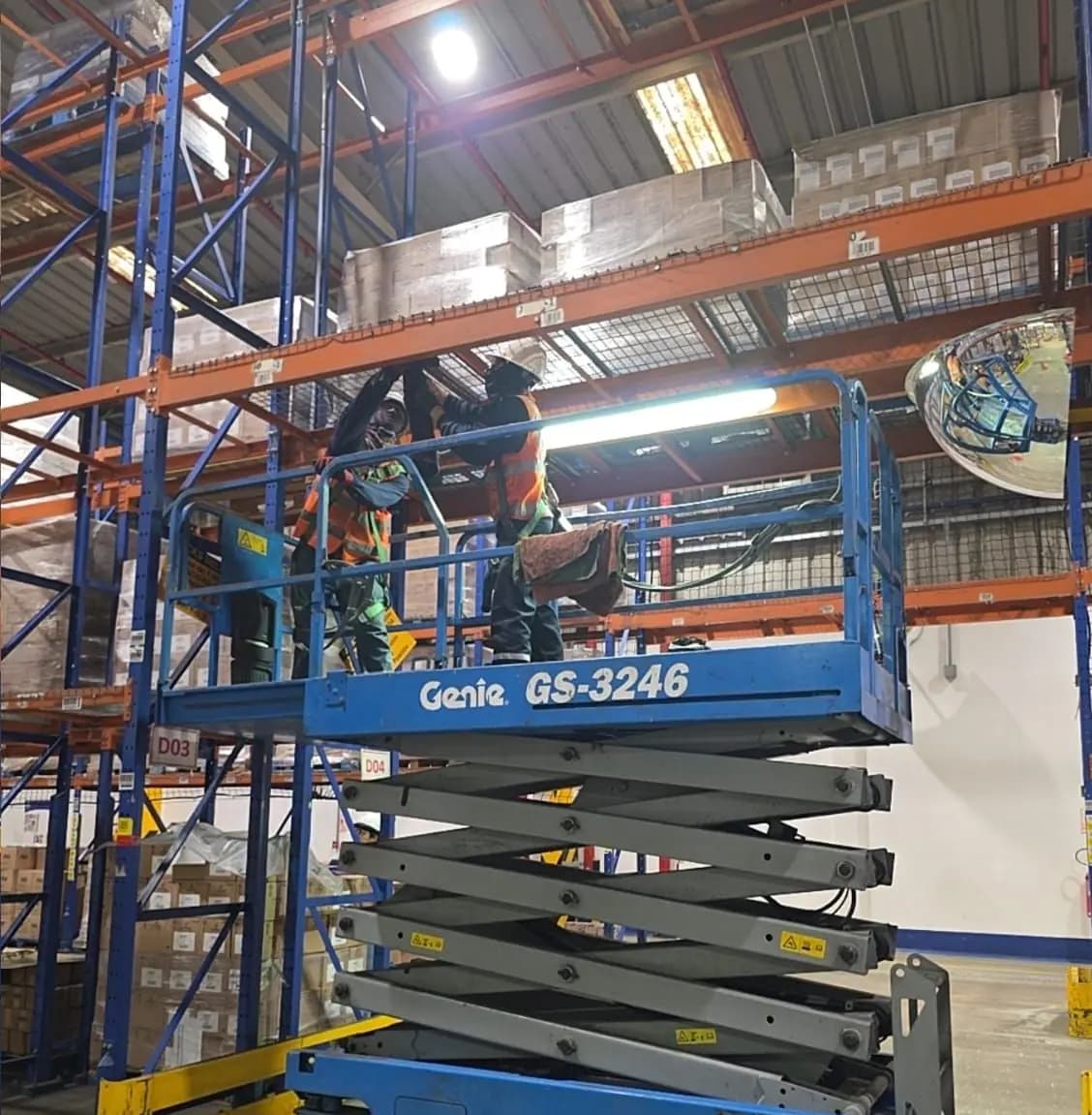 Plataforma de tijera elevando a técnicos para trabajo en altura entre racks de almacén